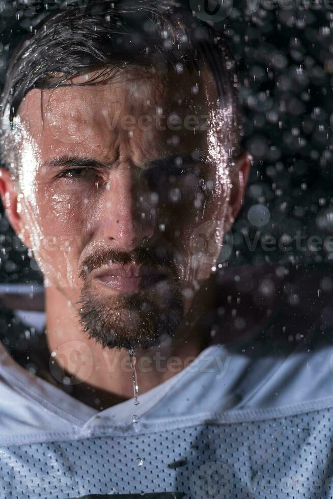 americano fútbol americano campo solitario atleta guerrero en pie en un campo sostiene su casco y Listo a jugar. jugador preparando a correr, ataque y Puntuación aterrizaje. lluvioso noche con dramático niebla, azul ligero foto