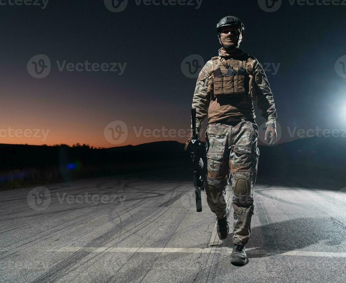 Ejército soldado en combate uniformes con un asalto rifle, plato portador y combate casco yendo en un peligroso misión en un lluvioso noche. foto