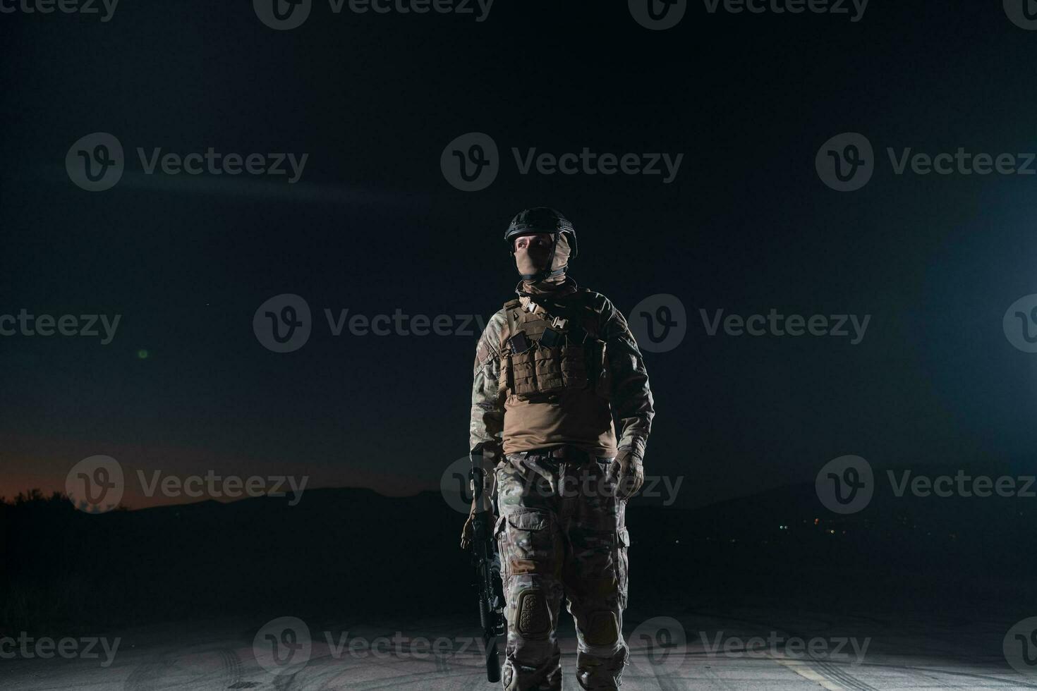 Army soldier in Combat Uniforms with an assault rifle, plate carrier and combat helmet going on a dangerous mission on a rainy night. photo