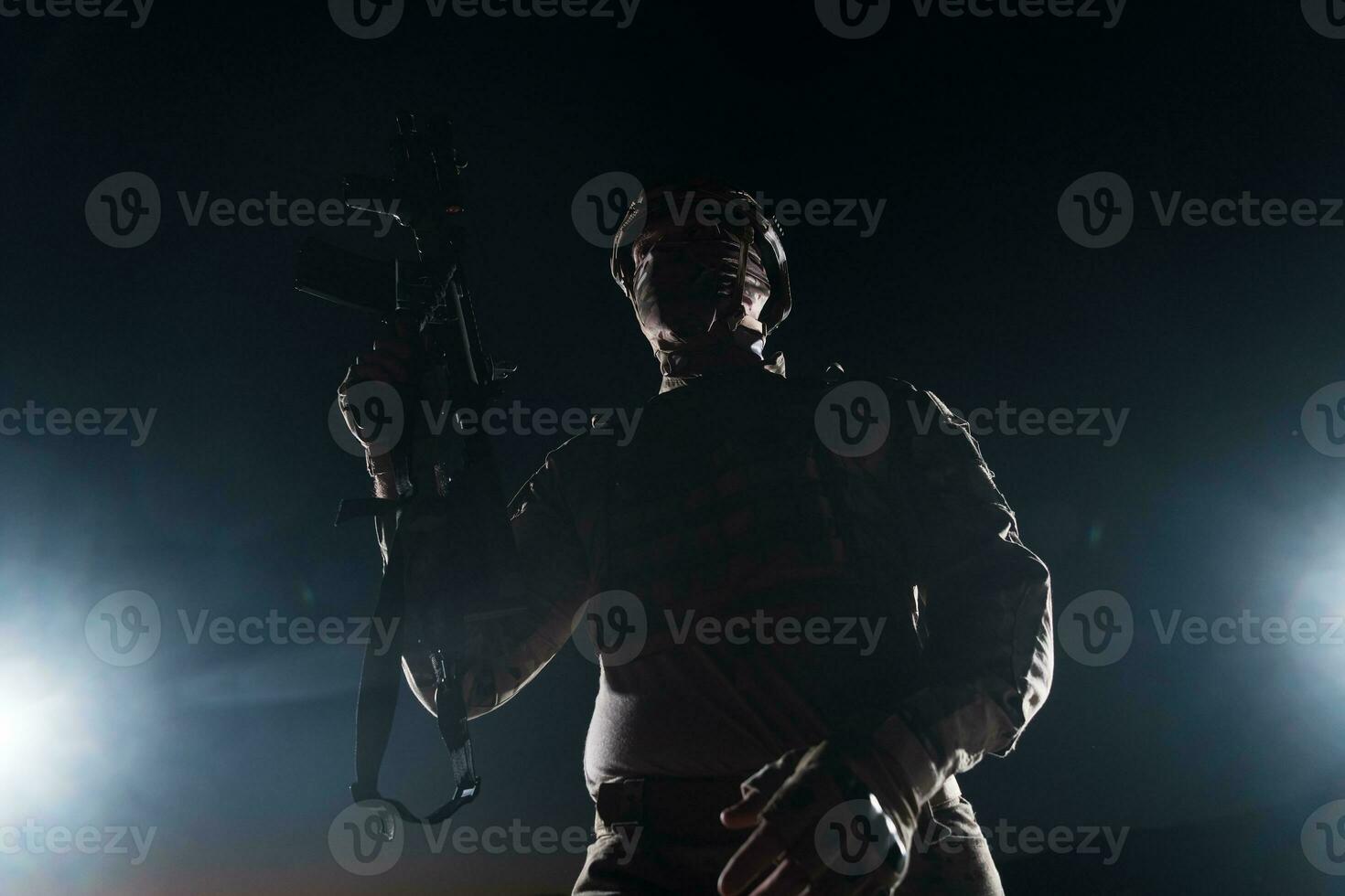 Army soldier in Combat Uniforms with an assault rifle, plate carrier and combat helmet going on a dangerous mission on a rainy night. photo