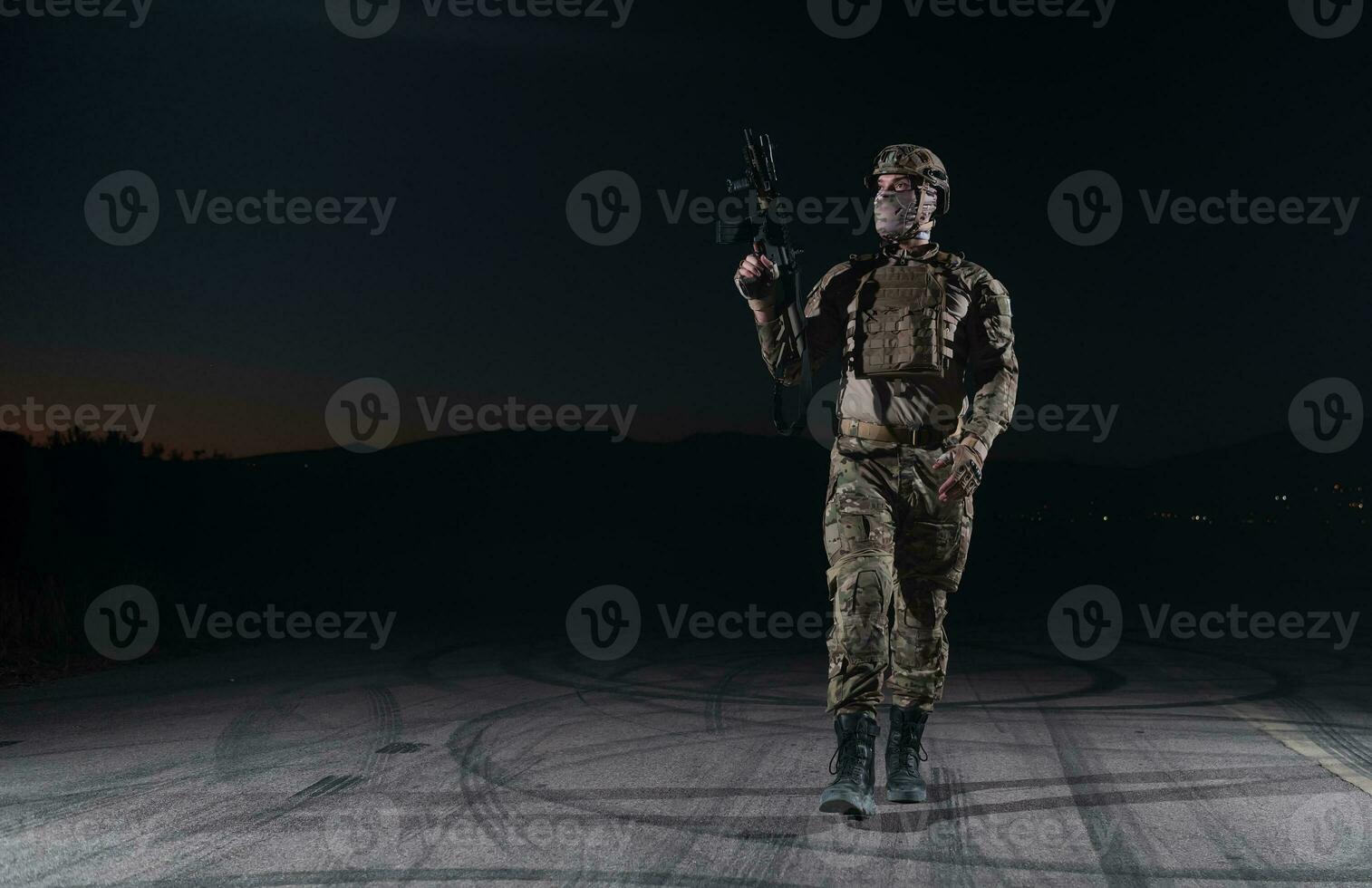 Army soldier in Combat Uniforms with an assault rifle, plate carrier and combat helmet going on a dangerous mission on a rainy night. photo