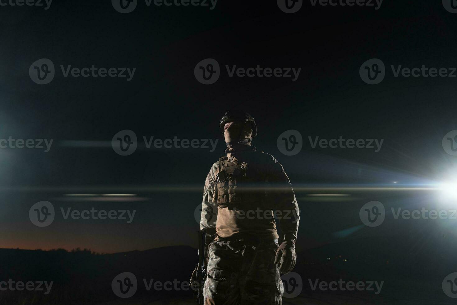 Army soldier in Combat Uniforms with an assault rifle, plate carrier and combat helmet going on a dangerous mission on a rainy night. photo