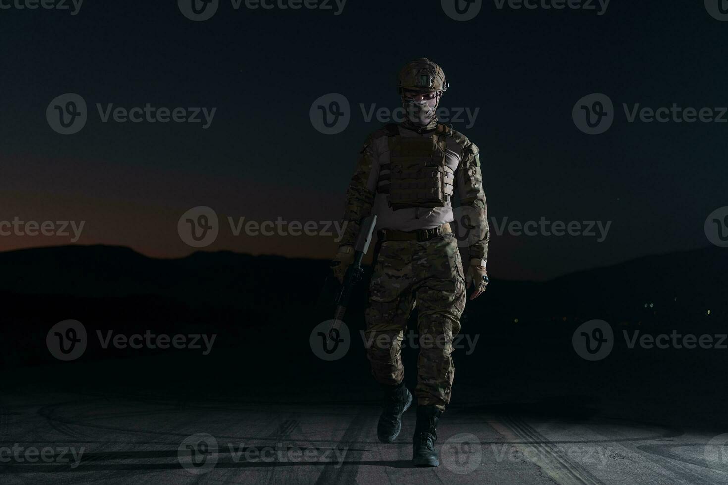 Army soldier in Combat Uniforms with an assault rifle, plate carrier and combat helmet going on a dangerous mission on a rainy night. photo