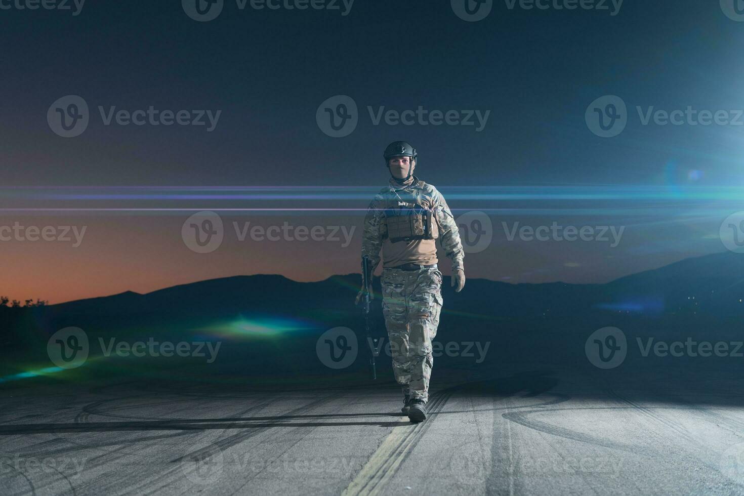 Army soldier in Combat Uniforms with an assault rifle, plate carrier and combat helmet going on a dangerous mission on a rainy night. photo