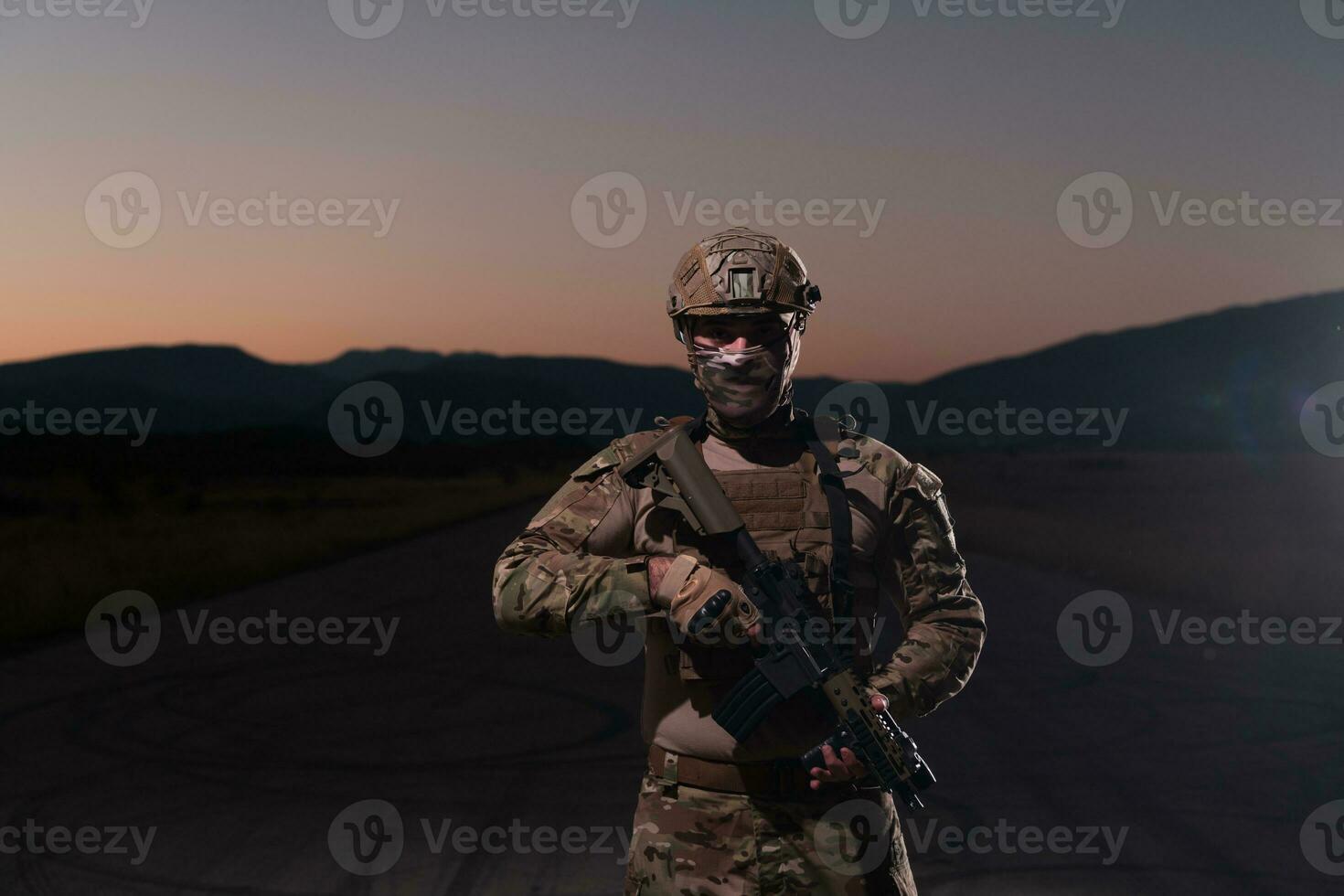 Army soldier in Combat Uniforms with an assault rifle, plate carrier and combat helmet going on a dangerous mission on a rainy night. photo
