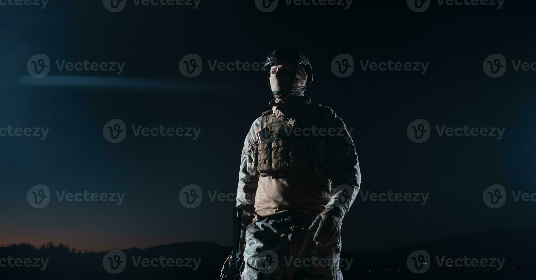 Army soldier in Combat Uniforms with an assault rifle, plate carrier and combat helmet going on a dangerous mission on a rainy night. photo