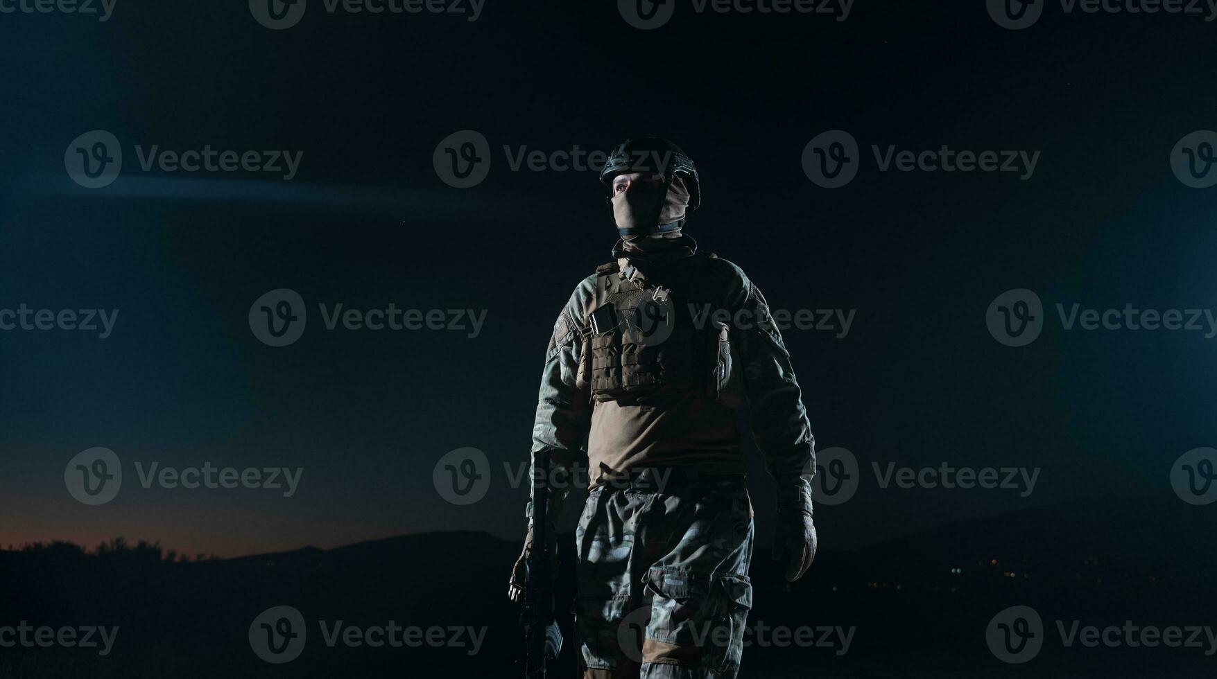 Army soldier in Combat Uniforms with an assault rifle, plate carrier and combat helmet going on a dangerous mission on a rainy night. photo