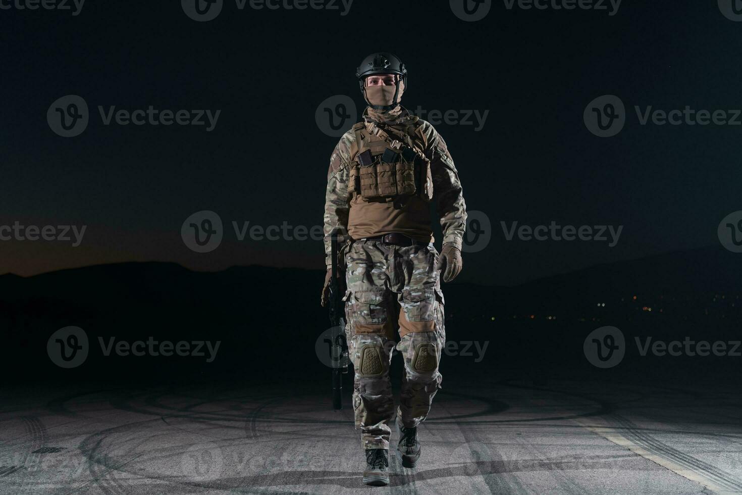 Army soldier in Combat Uniforms with an assault rifle, plate carrier and combat helmet going on a dangerous mission on a rainy night. photo