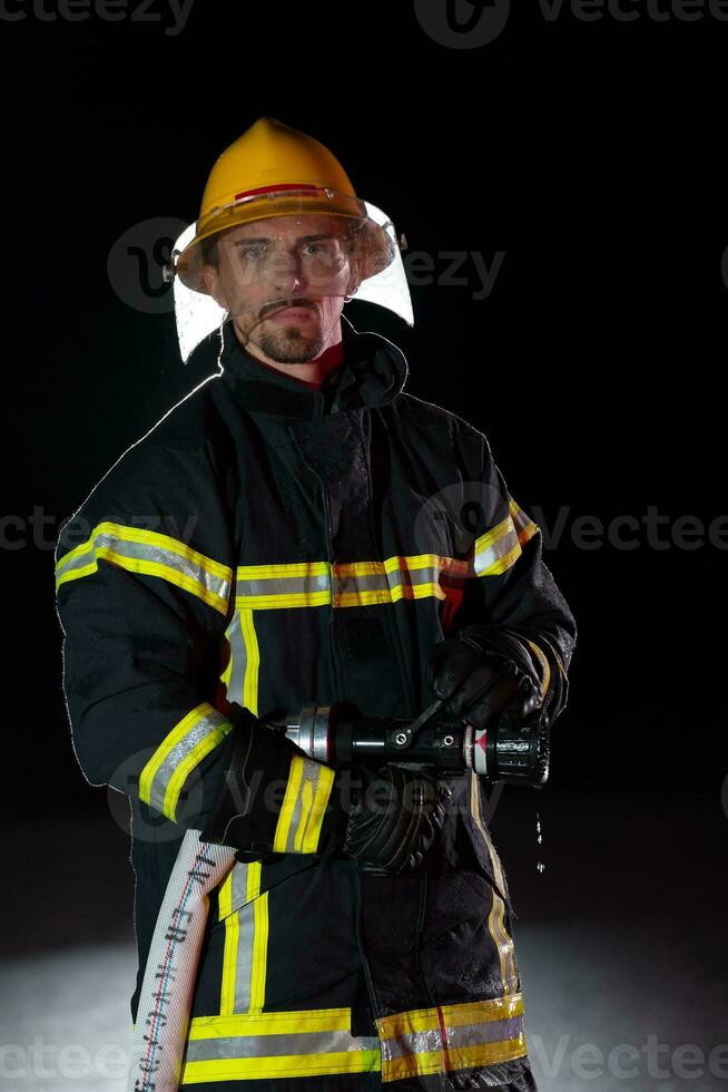 Firefighter in fire fighting operation. Portrait of a heroic fireman in a protective suit and red helmet in action during heavy rain. photo