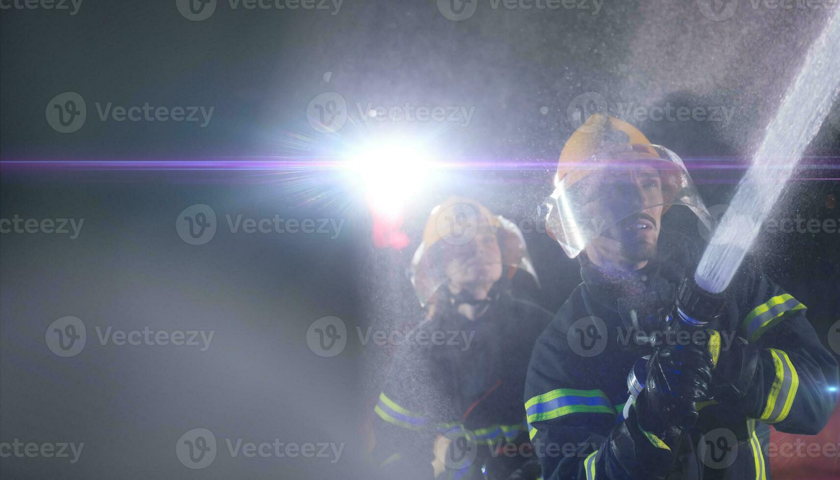 Firefighters using a water hose to eliminate a fire hazard. Team of female and male firemen in dangerous rescue mission. photo