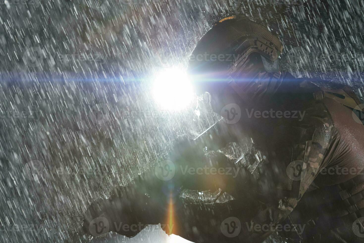 Army soldier in Combat Uniforms with an assault rifle, plate carrier and combat helmet going on a dangerous mission on a rainy night. photo