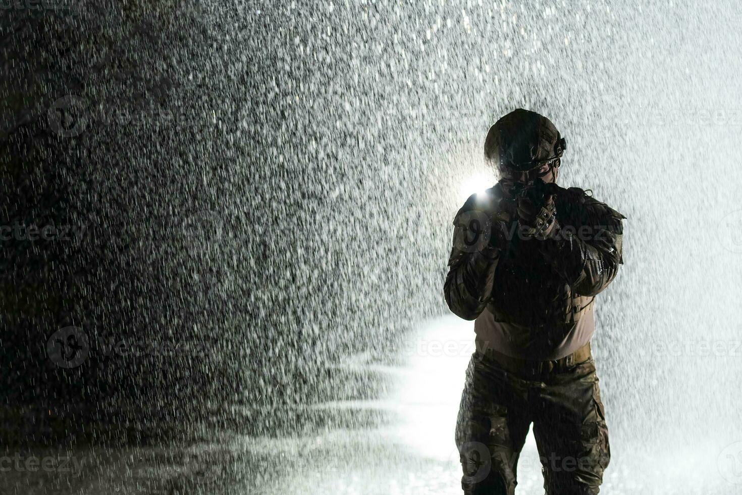 Army soldier in Combat Uniforms with an assault rifle, plate carrier and combat helmet going on a dangerous mission on a rainy night. photo