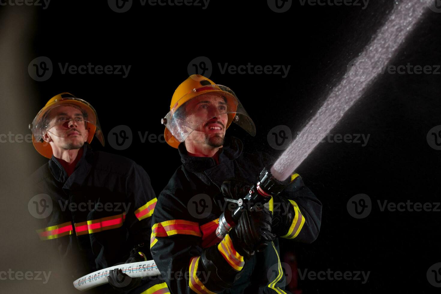 Firefighters use a water hose to eliminate a fire hazard. Team of firemen in the dangerous rescue mission. photo