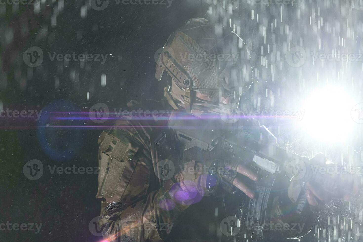 Army soldier in Combat Uniforms with an assault rifle, plate carrier and combat helmet going on a dangerous mission on a rainy night. photo