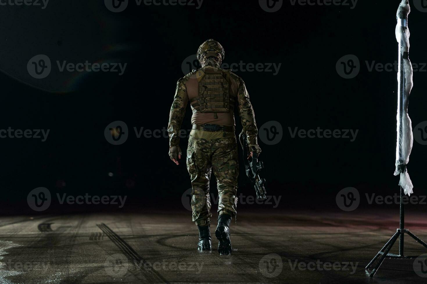 Army soldier in Combat Uniforms with an assault rifle, plate carrier and combat helmet going on a dangerous mission on a rainy night. photo