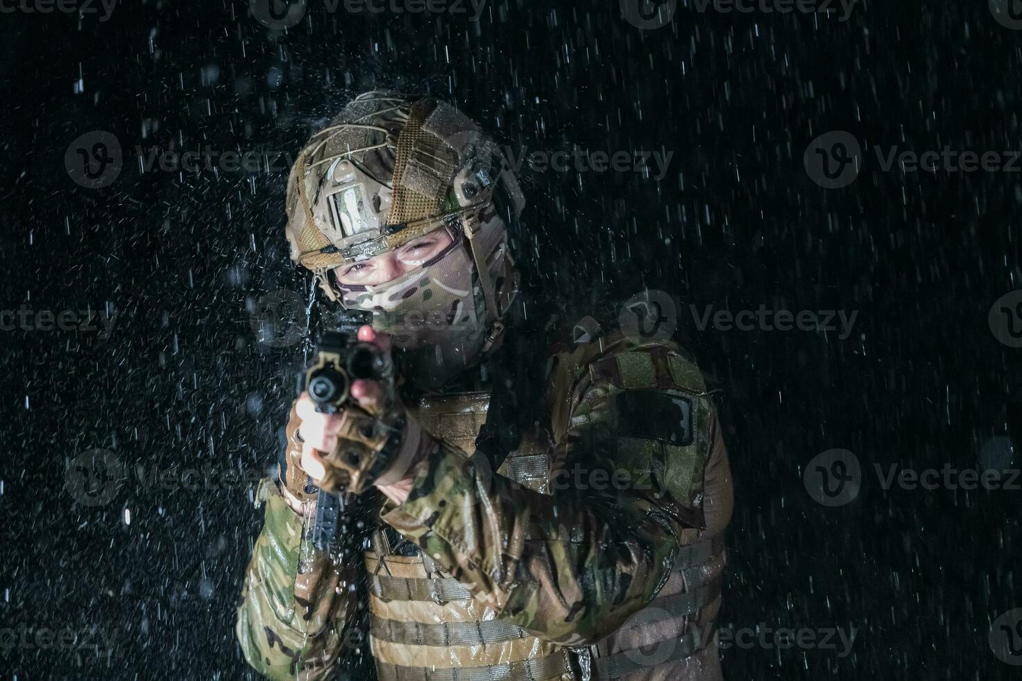 Army soldier in Combat Uniforms with an assault rifle, plate carrier and combat helmet going on a dangerous mission on a rainy night. photo