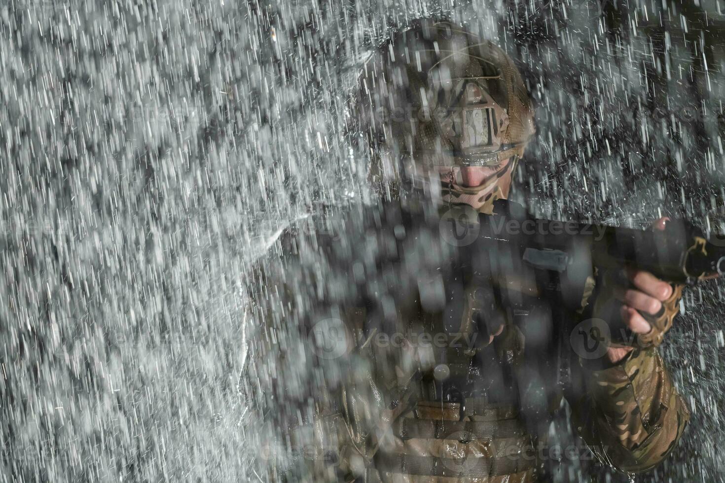 Army soldier in Combat Uniforms with an assault rifle, plate carrier and combat helmet going on a dangerous mission on a rainy night. photo