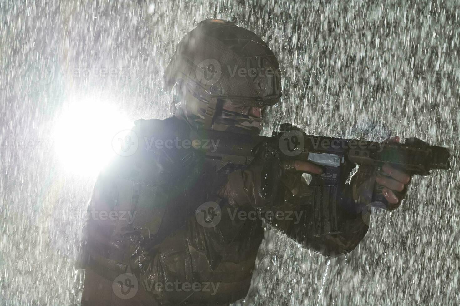 Army soldier in Combat Uniforms with an assault rifle, plate carrier and combat helmet going on a dangerous mission on a rainy night. photo