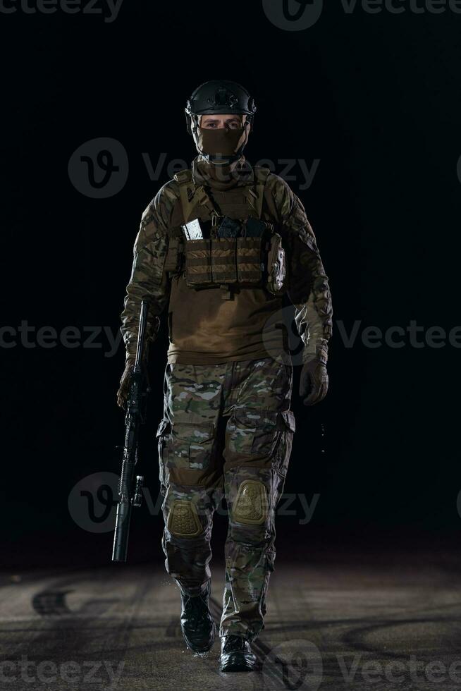 Army soldier in Combat Uniforms with an assault rifle, plate carrier and combat helmet going on a dangerous mission on a rainy night. photo