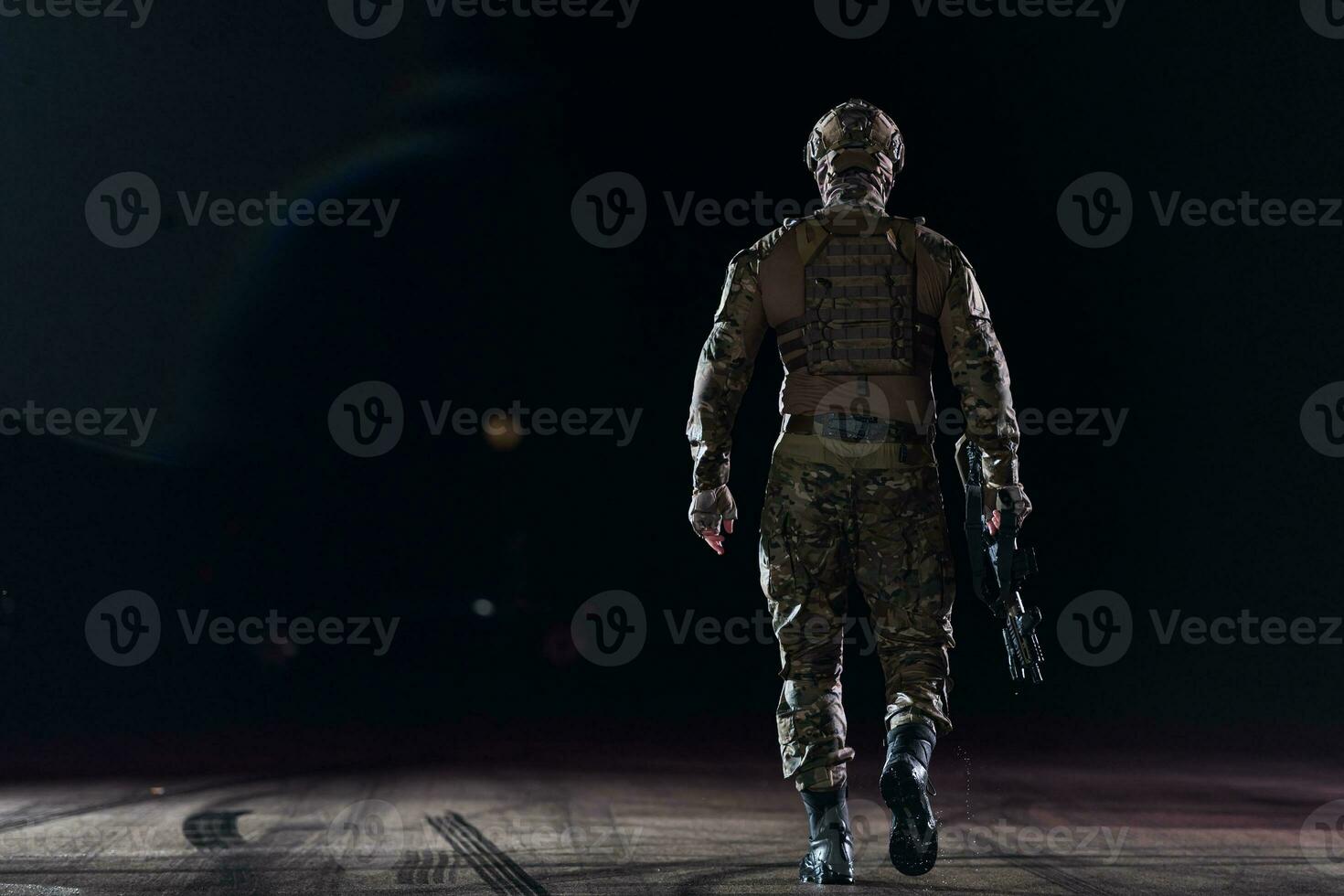 Ejército soldado en combate uniformes con un asalto rifle, plato portador y combate casco yendo en un peligroso misión en un lluvioso noche. foto