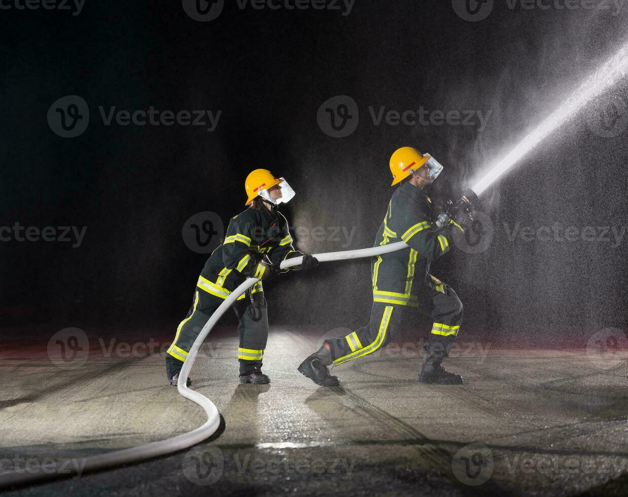 Firefighters using a water hose to eliminate a fire hazard. Team of female and male firemen in dangerous rescue mission. photo