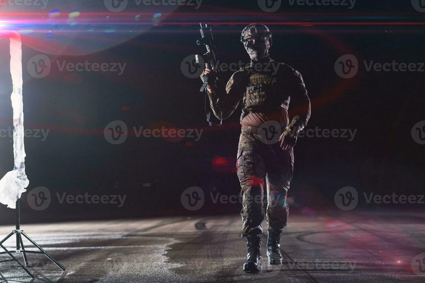 Army soldier in Combat Uniforms with an assault rifle, plate carrier and combat helmet going on a dangerous mission on a rainy night. photo