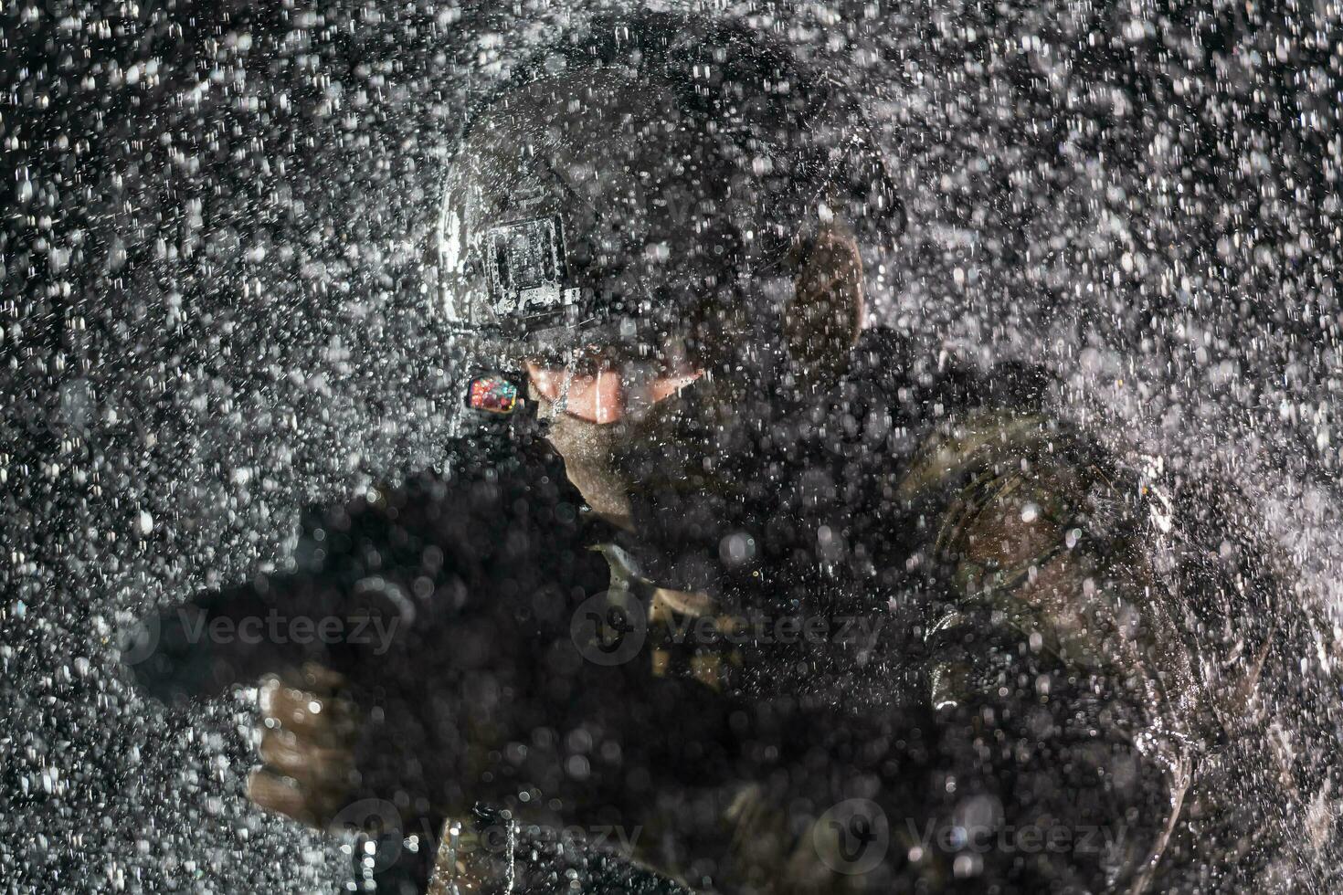 Army soldier in Combat Uniforms with an assault rifle, plate carrier and combat helmet going on a dangerous mission on a rainy night. photo