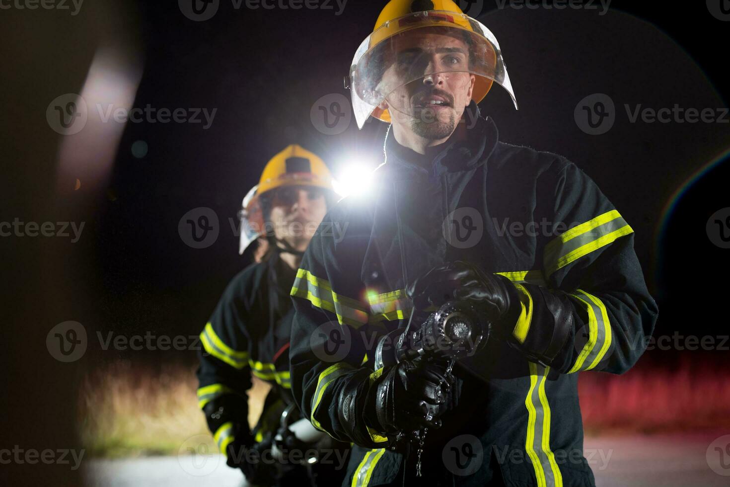 Firefighters using a water hose to eliminate a fire hazard. Team of female and male firemen in dangerous rescue mission. photo