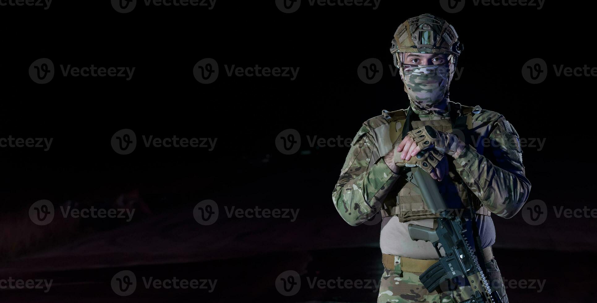 Army soldier in Combat Uniforms with an assault rifle, plate carrier and combat helmet going on a dangerous mission on a rainy night. photo