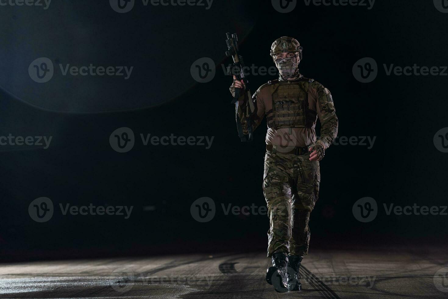 Army soldier in Combat Uniforms with an assault rifle, plate carrier and combat helmet going on a dangerous mission on a rainy night. photo
