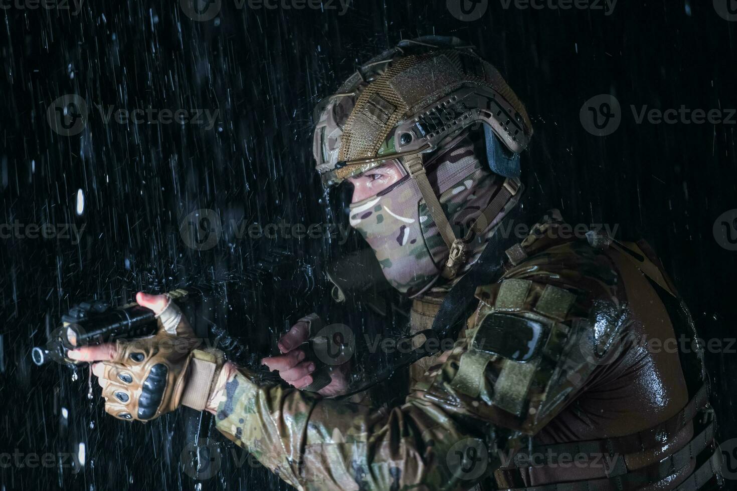 Army soldier in Combat Uniforms with an assault rifle, plate carrier and combat helmet going on a dangerous mission on a rainy night. photo