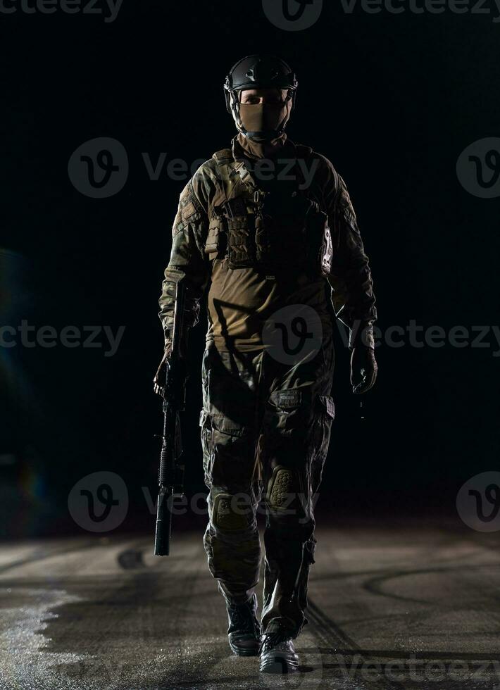 Ejército soldado en combate uniformes con un asalto rifle, plato portador y combate casco yendo en un peligroso misión en un lluvioso noche. foto