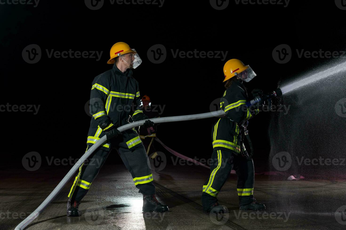 Firefighters using a water hose to eliminate a fire hazard. Team of female and male firemen in dangerous rescue mission. photo