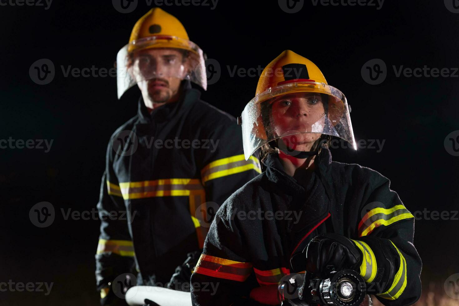 Firefighters using a water hose to eliminate a fire hazard. Team of female and male firemen in dangerous rescue mission. photo