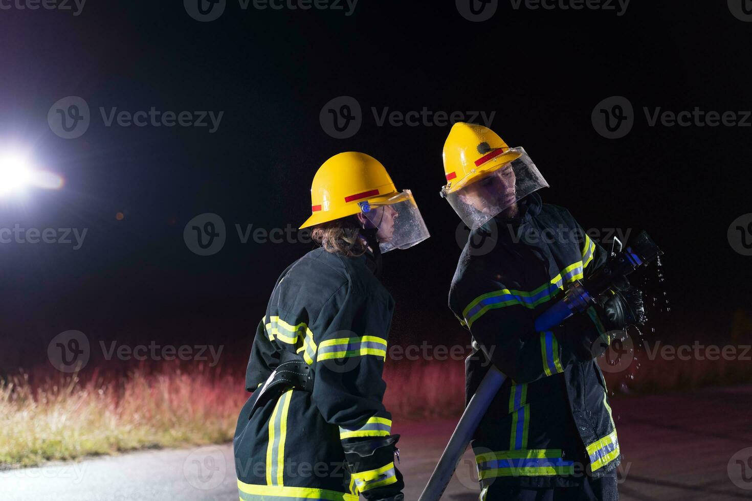 Firefighters using a water hose to eliminate a fire hazard. Team of female and male firemen in dangerous rescue mission. photo