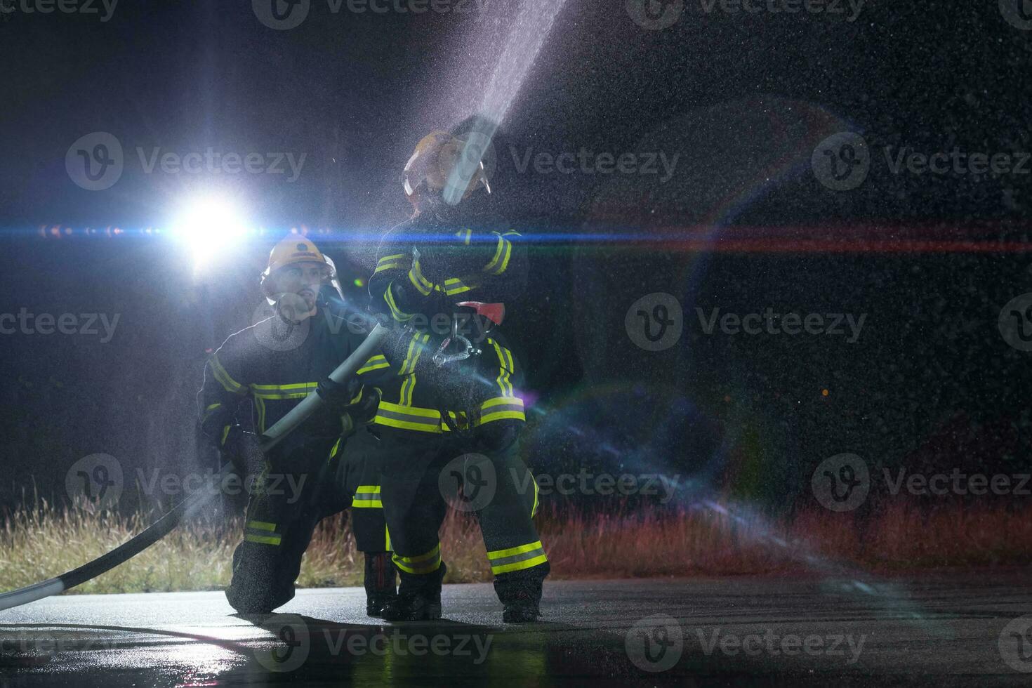 Firefighters using a water hose to eliminate a fire hazard. Team of female and male firemen in dangerous rescue mission. photo