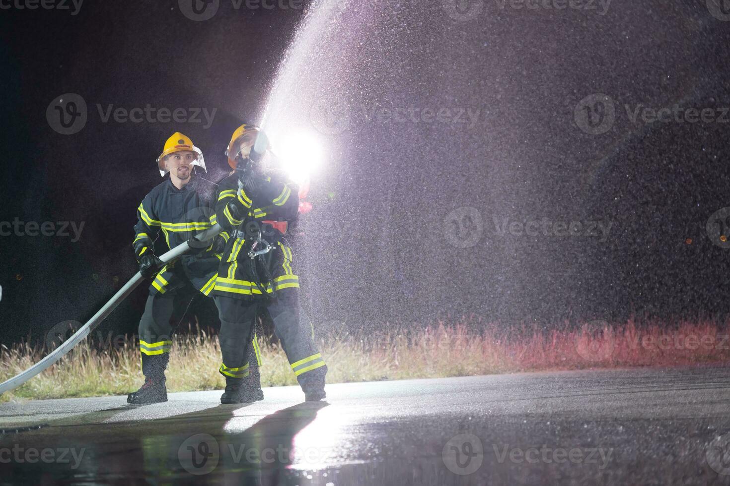 bomberos utilizando un agua manguera a eliminar un fuego peligro. equipo de hembra y masculino bomberos en peligroso rescate misión. foto