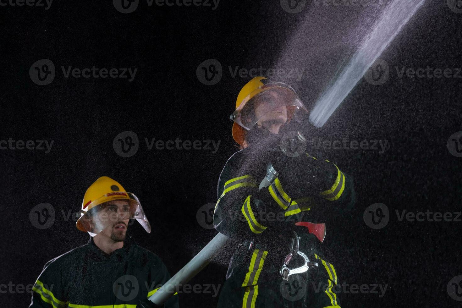 Firefighters using a water hose to eliminate a fire hazard. Team of female and male firemen in dangerous rescue mission. photo