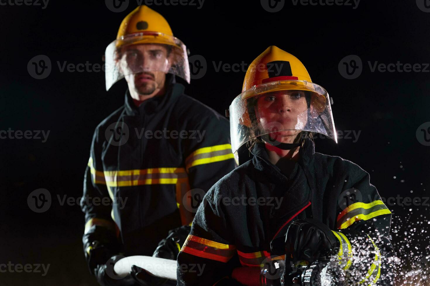 Firefighters using a water hose to eliminate a fire hazard. Team of female and male firemen in dangerous rescue mission. photo