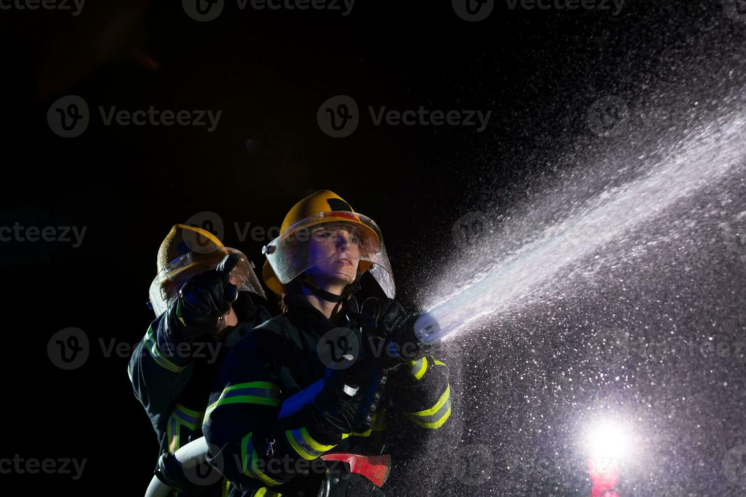 bomberos utilizando un agua manguera a eliminar un fuego peligro. equipo de hembra y masculino bomberos en peligroso rescate misión. foto