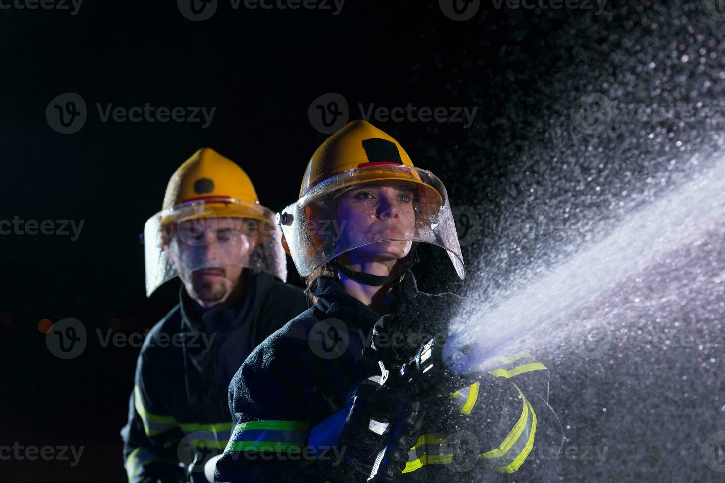 Firefighters using a water hose to eliminate a fire hazard. Team of female and male firemen in dangerous rescue mission. photo