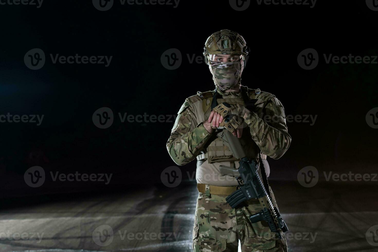 Army soldier in Combat Uniforms with an assault rifle, plate carrier and combat helmet going on a dangerous mission on a rainy night. photo