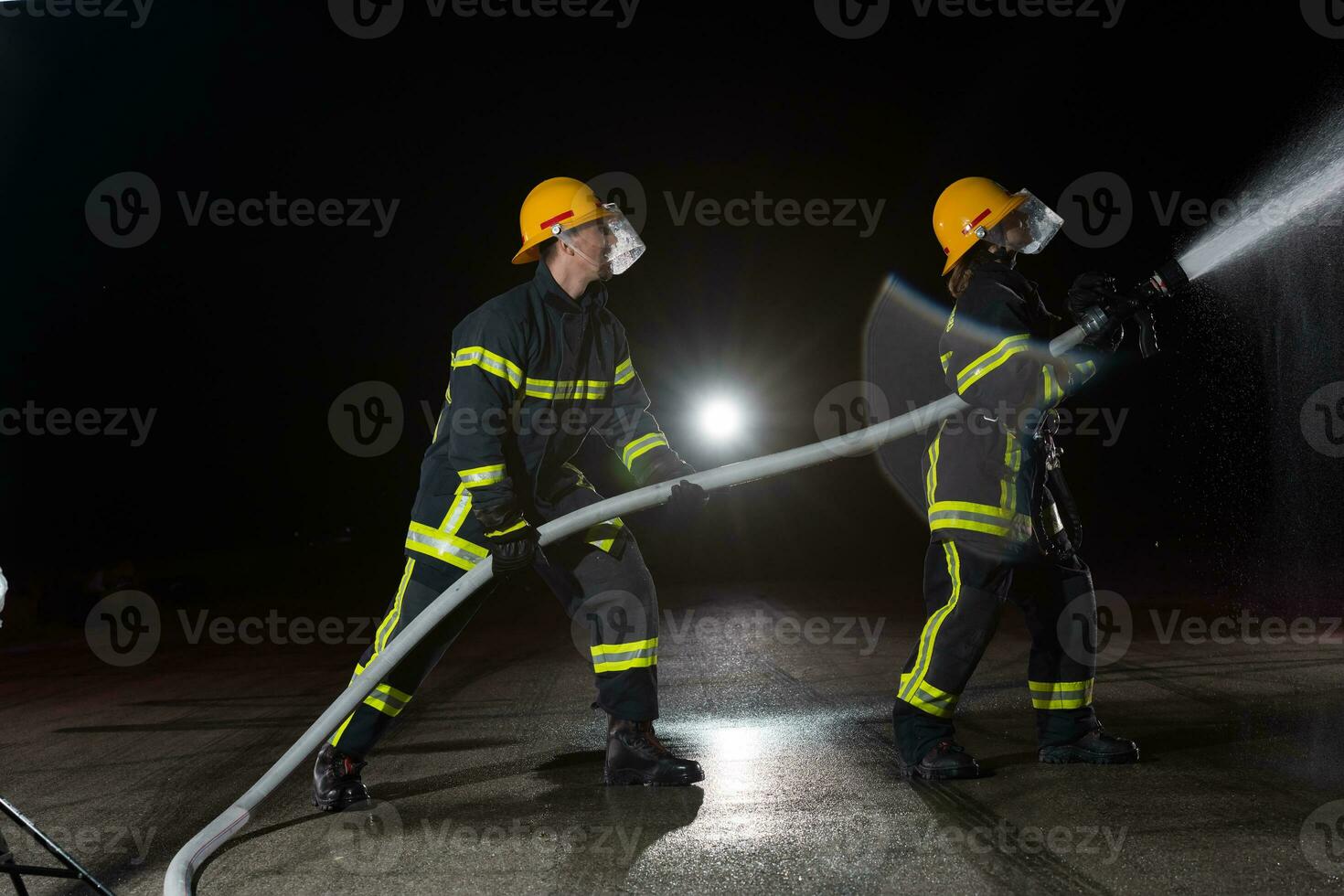 Firefighters using a water hose to eliminate a fire hazard. Team of female and male firemen in dangerous rescue mission. photo