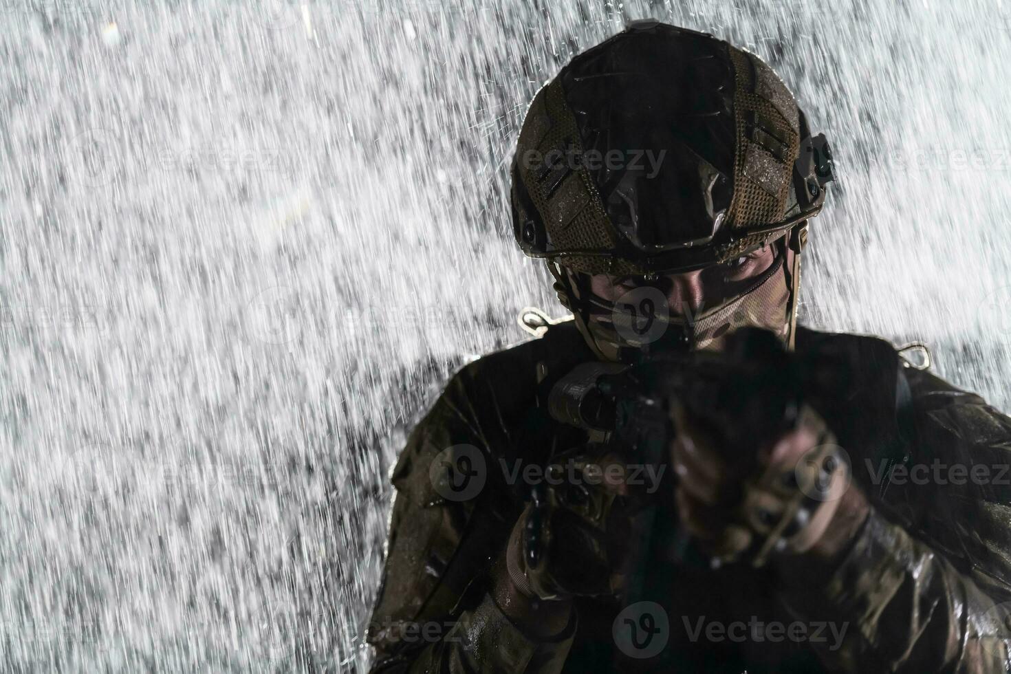 Army soldier in Combat Uniforms with an assault rifle, plate carrier and combat helmet going on a dangerous mission on a rainy night. photo