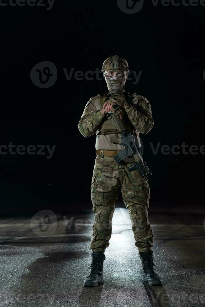 Army soldier in Combat Uniforms with an assault rifle, plate carrier and combat helmet going on a dangerous mission on a rainy night. photo