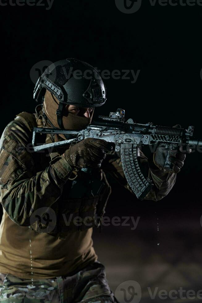 Ejército soldado en combate uniformes con un asalto rifle, plato portador y combate casco yendo en un peligroso misión en un lluvioso noche. foto