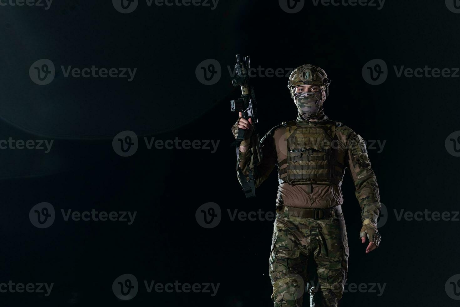 Army soldier in Combat Uniforms with an assault rifle, plate carrier and combat helmet going on a dangerous mission on a rainy night. photo