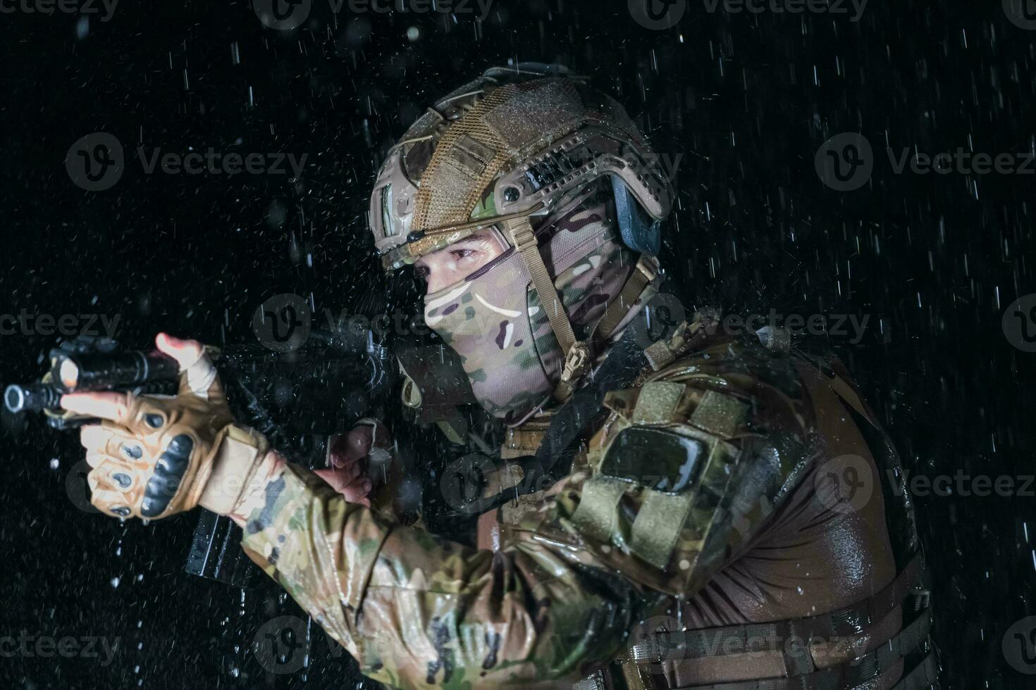 Army soldier in Combat Uniforms with an assault rifle, plate carrier and combat helmet going on a dangerous mission on a rainy night. photo