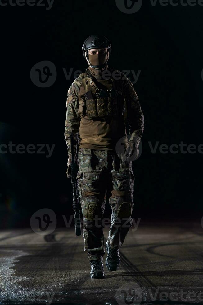 Ejército soldado en combate uniformes con un asalto rifle, plato portador y combate casco yendo en un peligroso misión en un lluvioso noche. foto