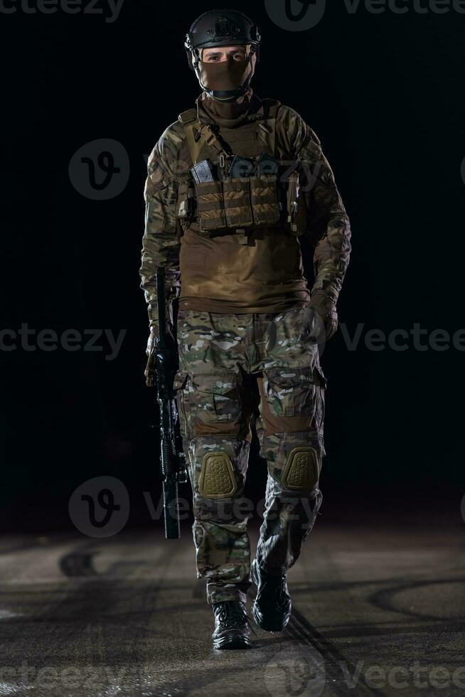 Army soldier in Combat Uniforms with an assault rifle, plate carrier and combat helmet going on a dangerous mission on a rainy night. photo